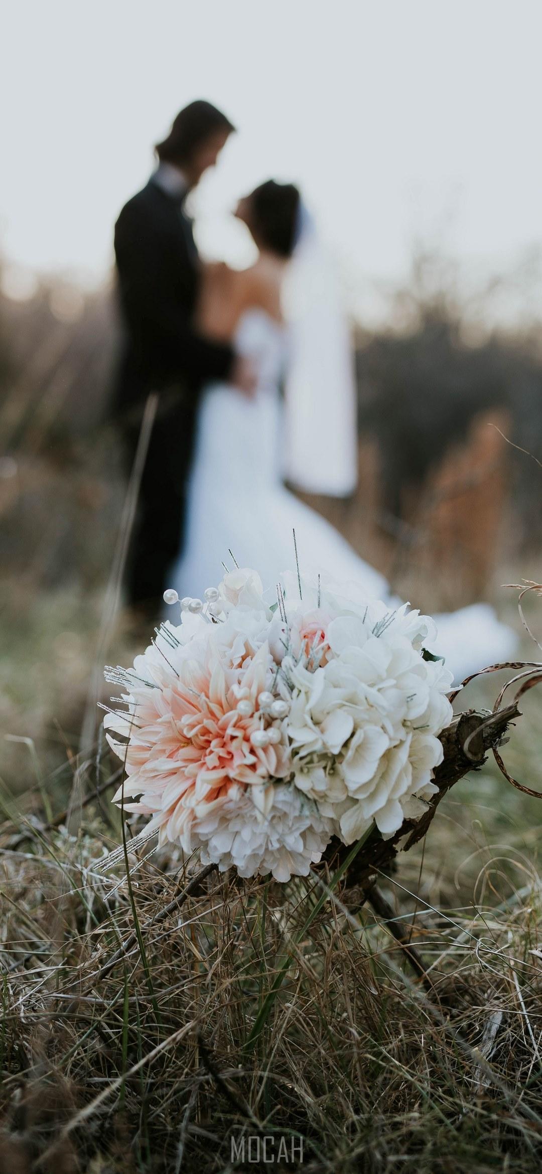 HD wallpaper, Wedding Evening, 1080X2340, A Bouquet Sits In Tall Grass While A Married Couple Embraces In The Fuzzy Background, Lenovo Legion Duel Wallpaper 1080P