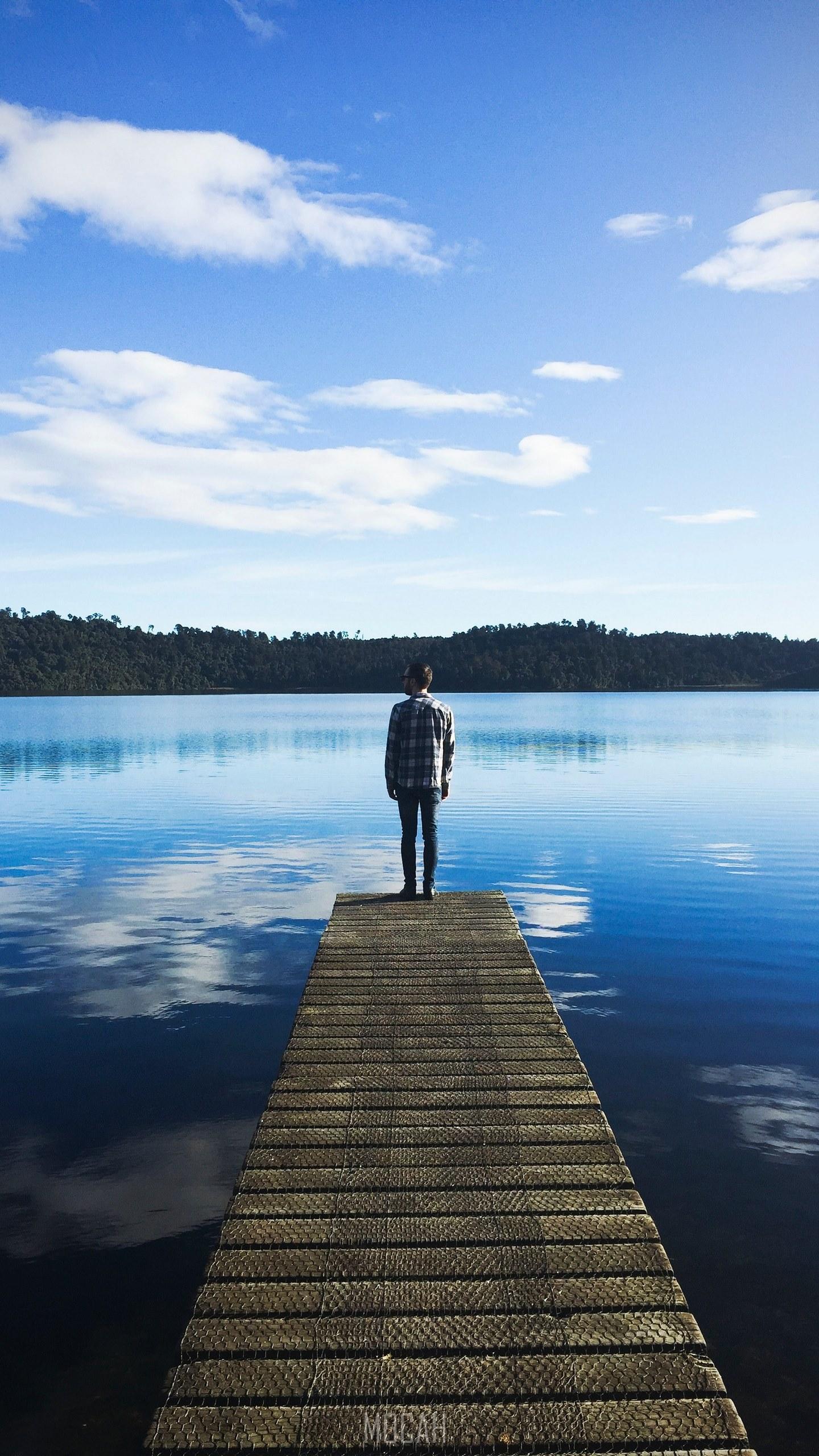 HD wallpaper, On The Piers Edge, A Man Wearing A Flannel Standing On The Edge Of A Dock On A Lake That Is Reflecting The Blue Sky And Clouds, Lg Q8 Screensaver, 1440X2560
