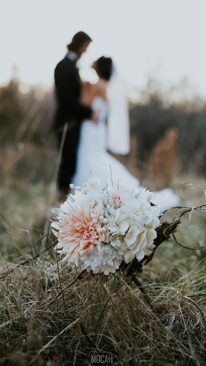 HD wallpaper, 720X1280, A Bouquet Sits In Tall Grass While A Married Couple Embraces In The Fuzzy Background, Wedding Evening, Nokia 2 Full Hd Wallpaper