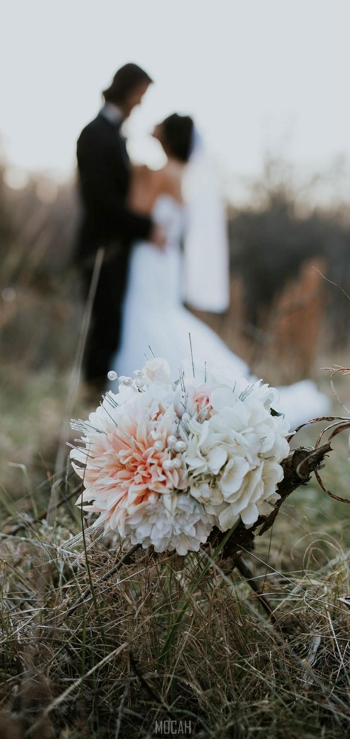 HD wallpaper, Honor 8S 2020 Screensaver, Wedding Evening, A Bouquet Sits In Tall Grass While A Married Couple Embraces In The Fuzzy Background, 720X1520