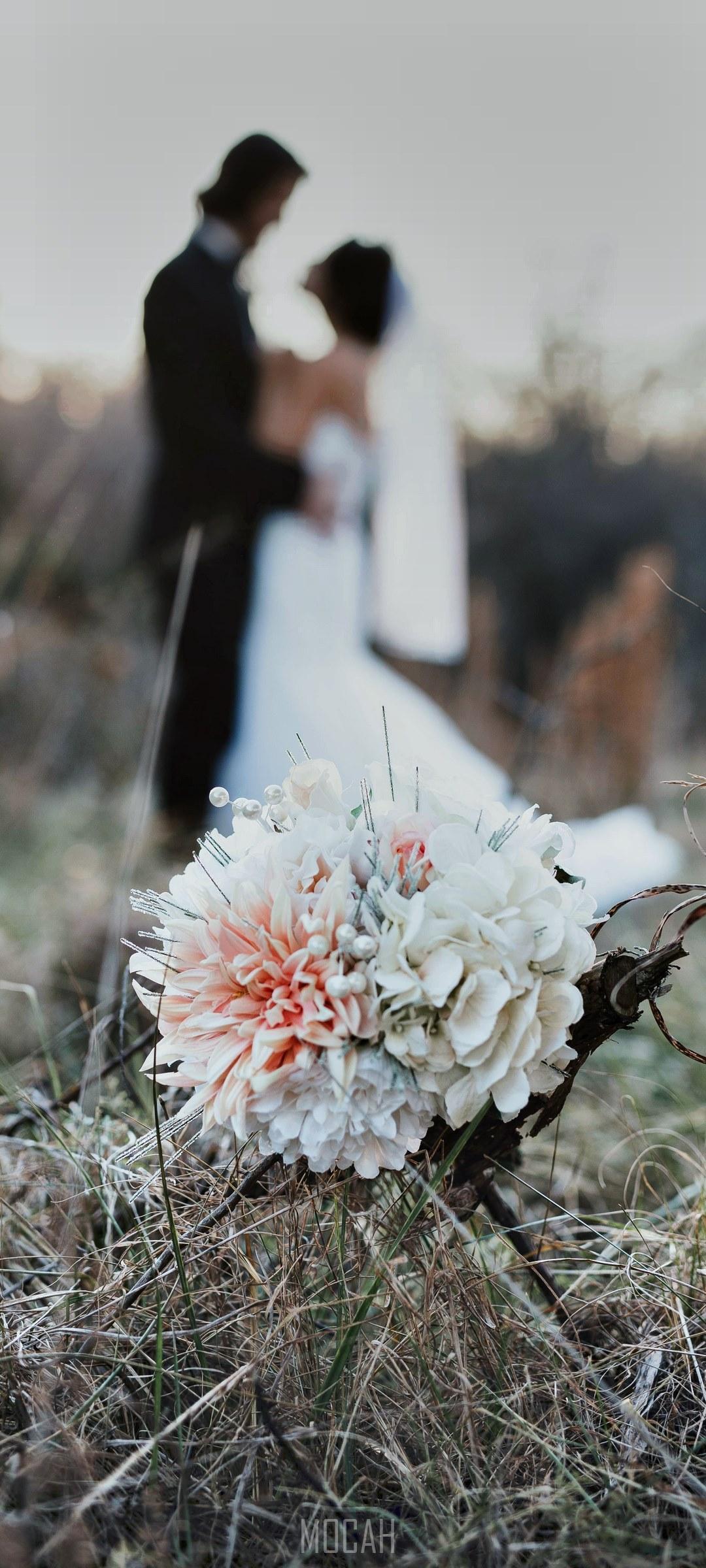 HD wallpaper, Wedding Evening, A Bouquet Sits In Tall Grass While A Married Couple Embraces In The Fuzzy Background, Honor 30S Screensaver, 1080X2400
